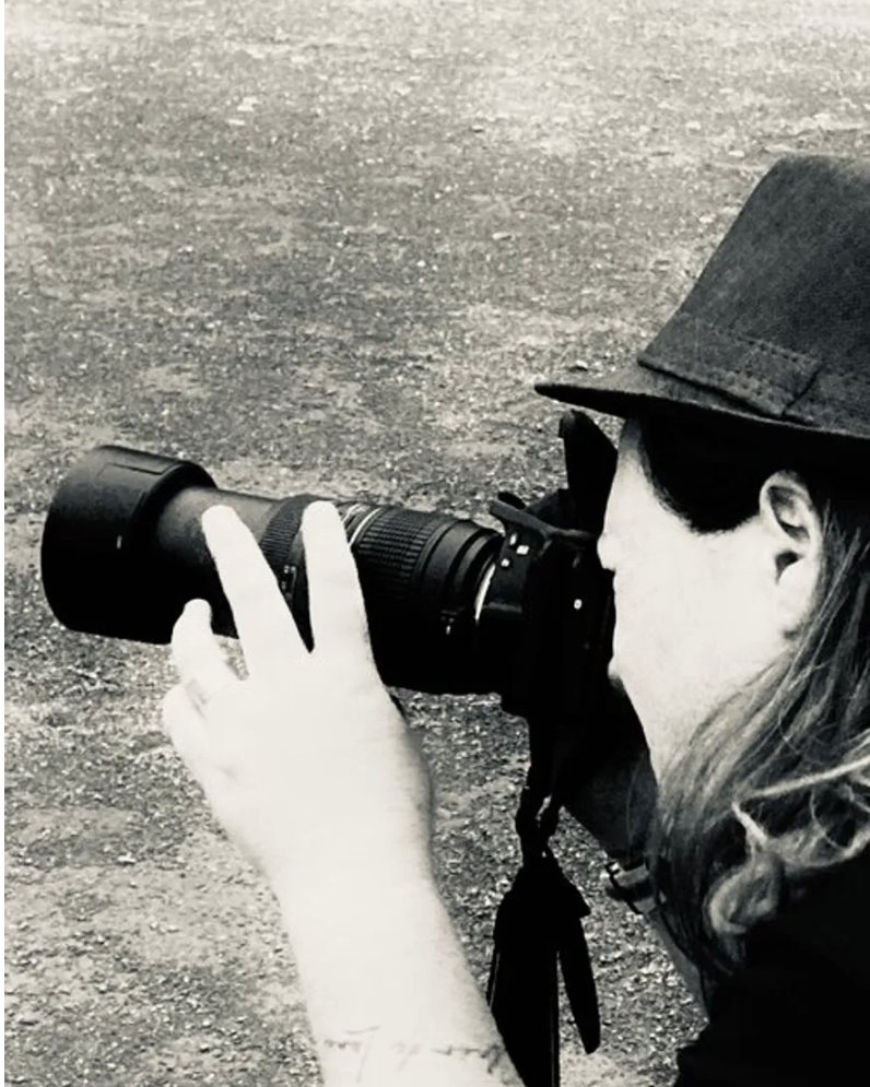 Christelle Duval en train de photographier, appareil à la main, chapeau et lunettes noires